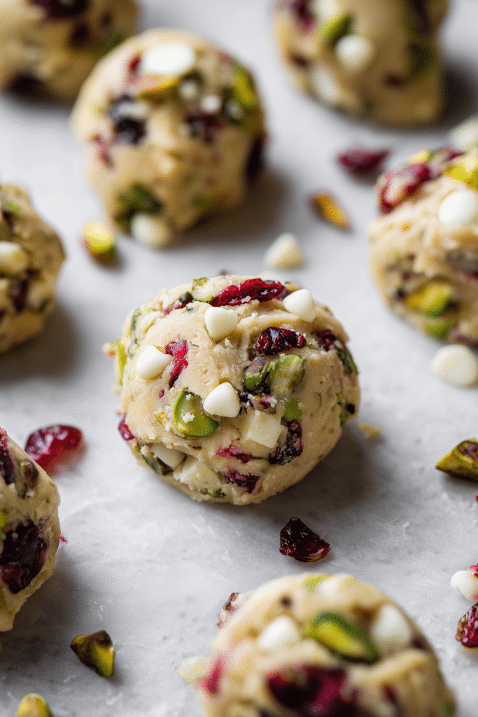 Scooped Pistachio Cranberry Cookie dough on parchment, filled with pistachios and cranberries.