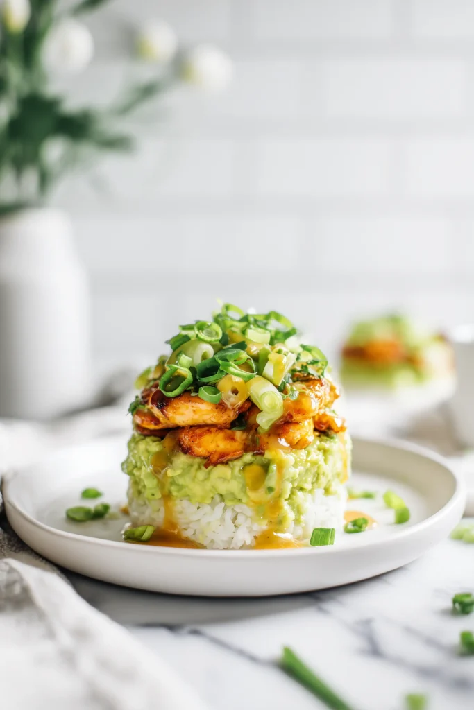 A vibrant stack of honey lime chicken, creamy avocado, and citrusy rice, garnished and drizzled, perfectly representing Honey Lime Chicken and Avocado Rice Stack.