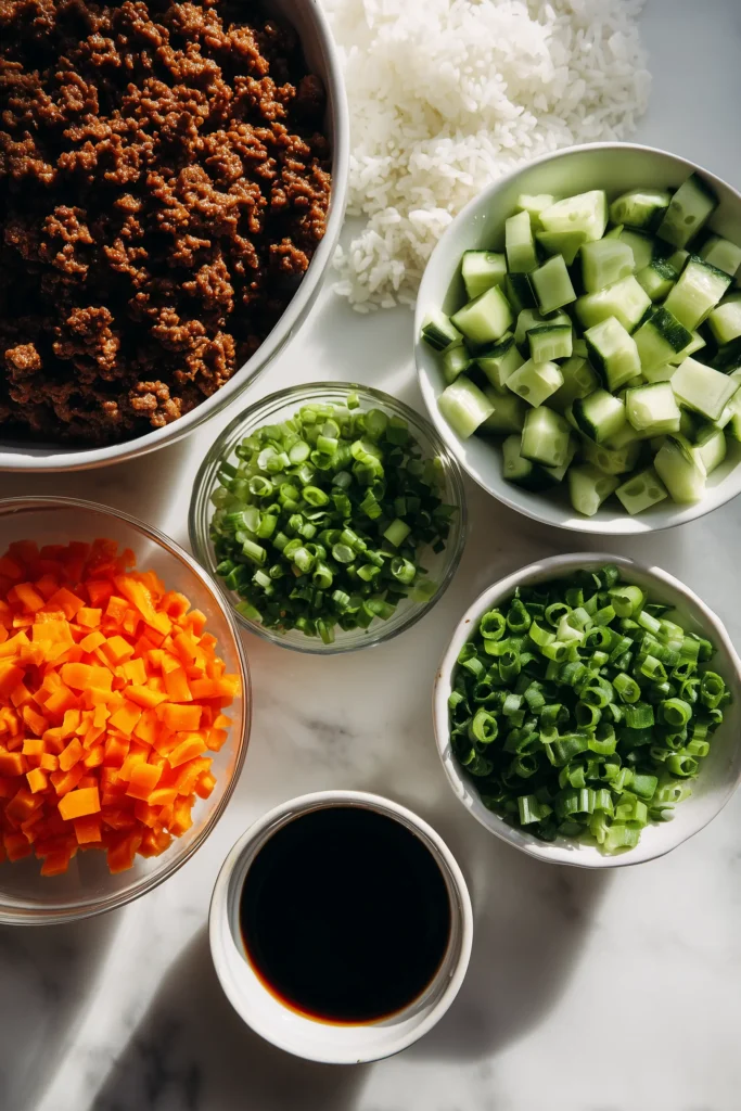 Korean Ground Beef Bowl 2 Bowls and piles of ground beef, rice, fresh vegetables, and sauces set out for Korean Ground Beef Bowl.