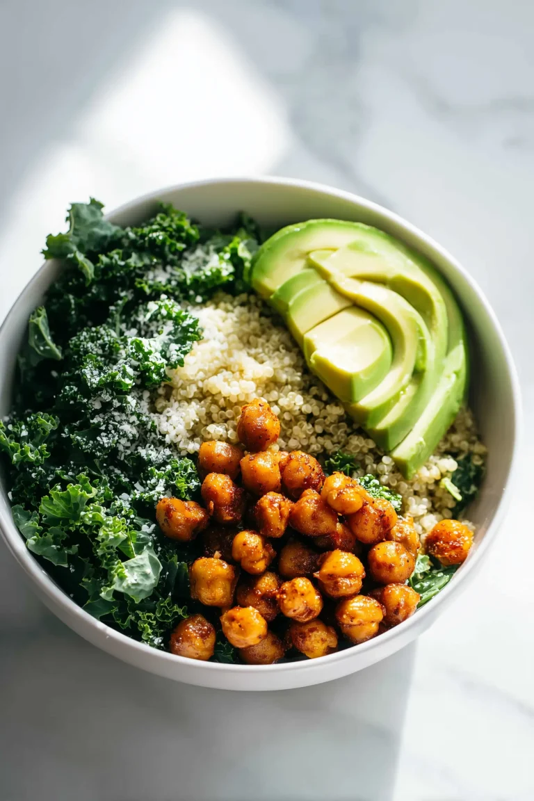 A bowl of Lemony Quinoa Kale Salad with kale, quinoa, roasted chickpeas, and avocado on a bright marble surface.