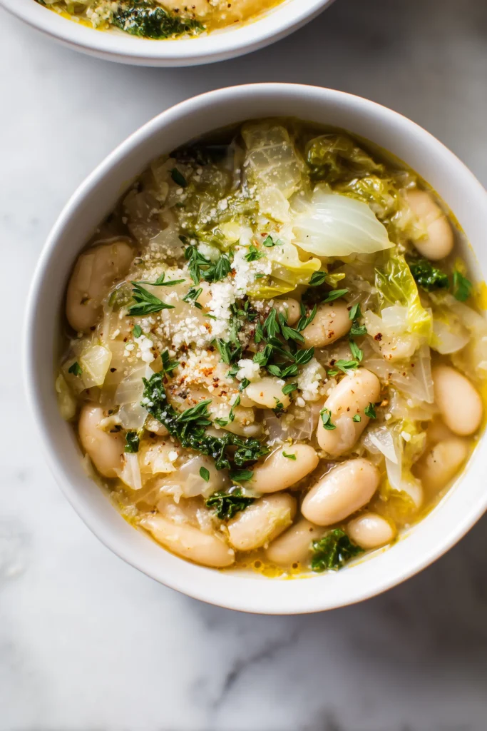 A bowl filled with White Bean Escarole Soup showing creamy white beans, escarole, and golden broth.