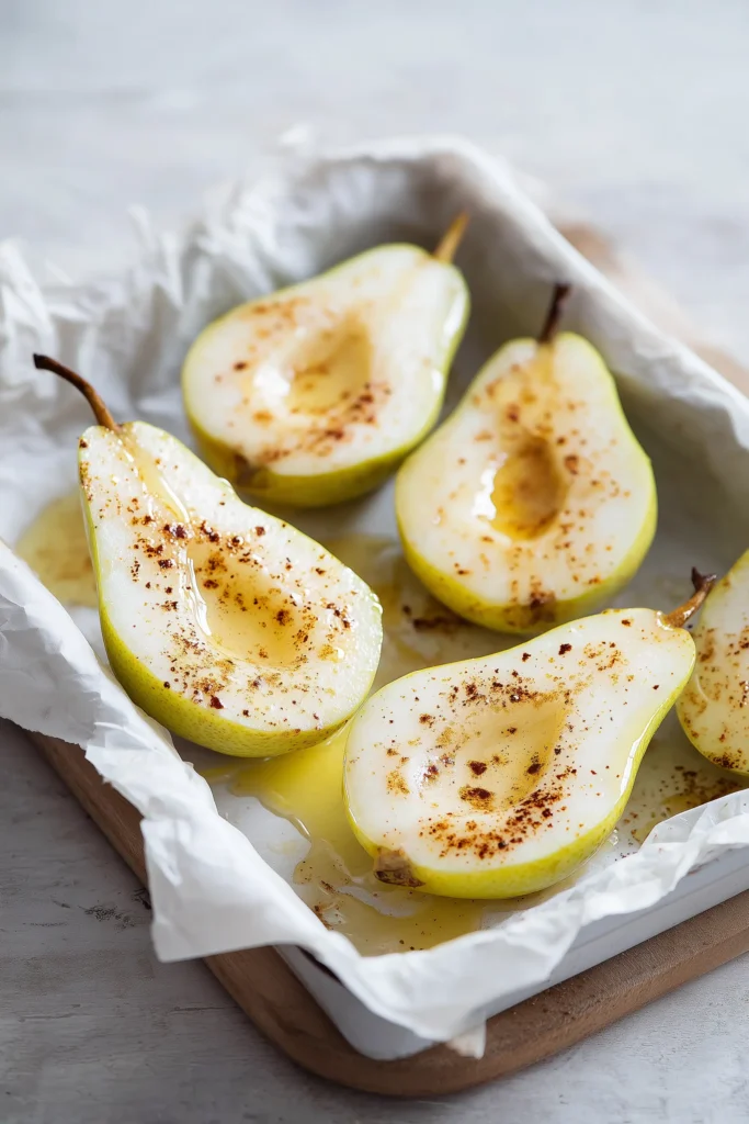 Halved pears in a baking dish, brushed with butter and cinnamon for Baked Pears Feta Honey Cranberries.
