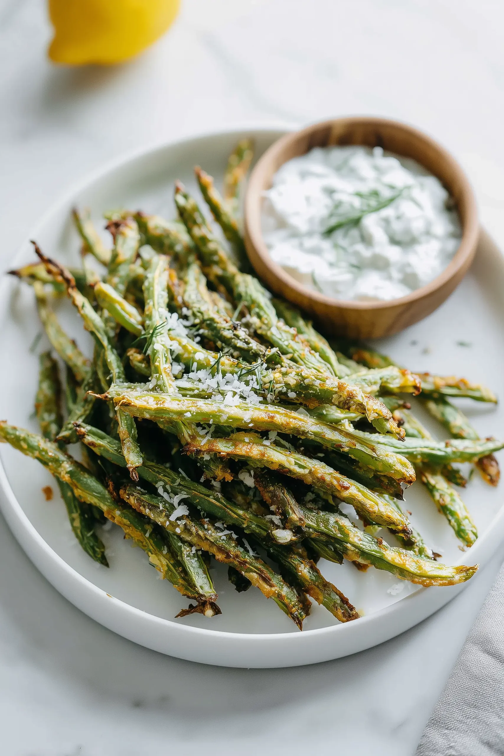 A plate of Crispy Oven Baked Green Beans with Parmesan, golden and crunchy, next to a bowl of yogurt dip.