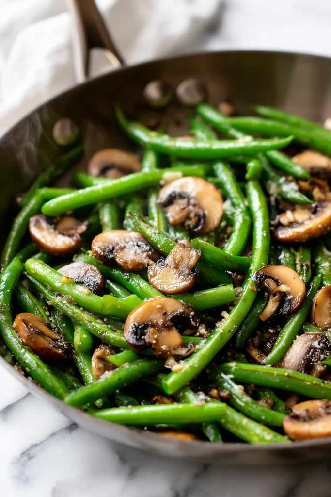 Close-up photo of green beans and mushrooms sautéing in garlic butter in a skillet, showing crisp colors and glistening texture.