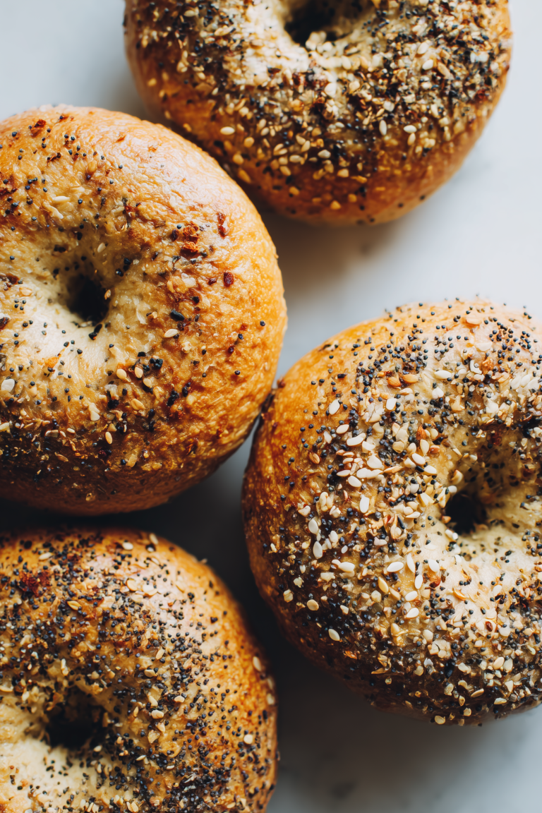 Golden New York Style Bagels stacked on a marble background, showcasing their shiny crust and soft crumb.