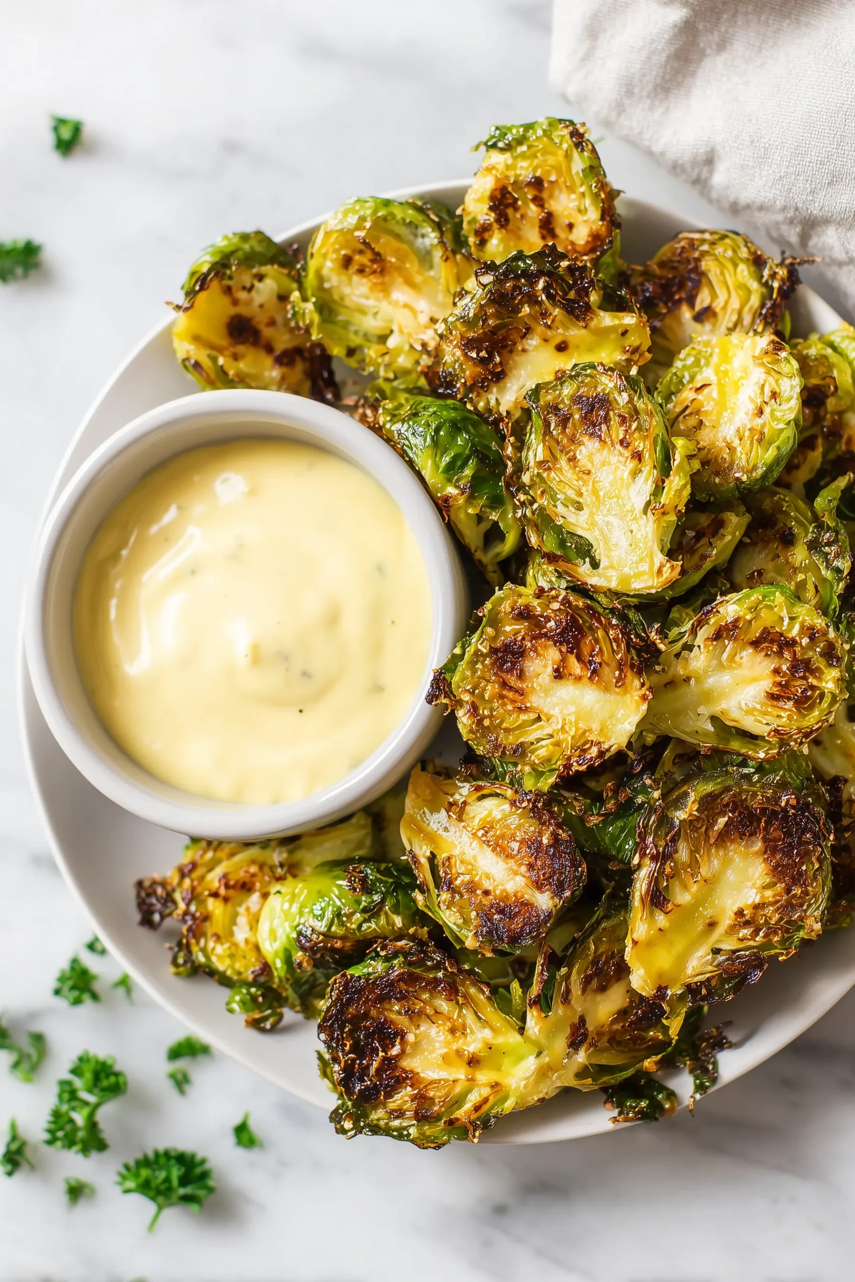 A plate of Crispy Brussel Sprouts With Dijon Aioli, golden and crispy, arranged next to a creamy dipping sauce.
