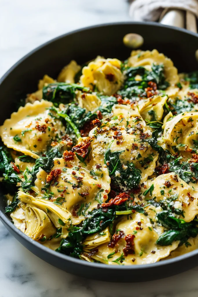Close-up of creamy ravioli with spinach, artichokes, capers, sun-dried tomatoes and herbs in a skillet.