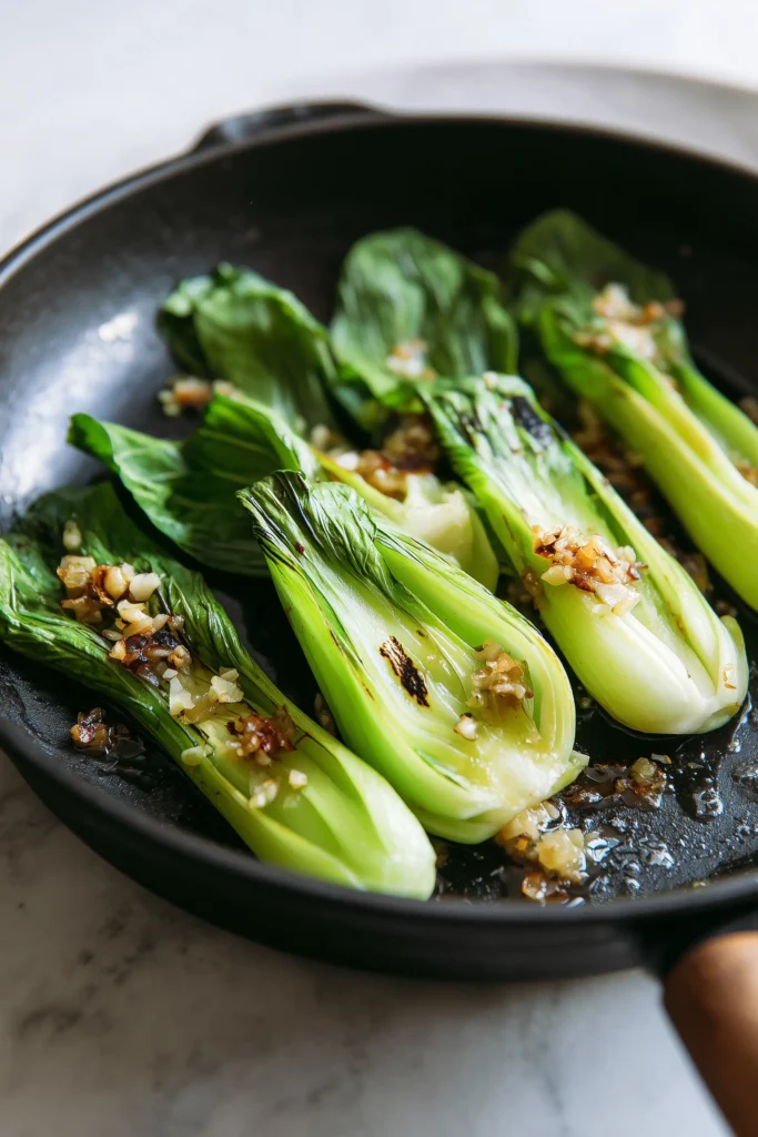 Garlic Ginger Bok Choy 3 Bright process photo of Garlic Ginger Bok Choy being sautéed with garlic and ginger, stalks turning golden in the skillet.