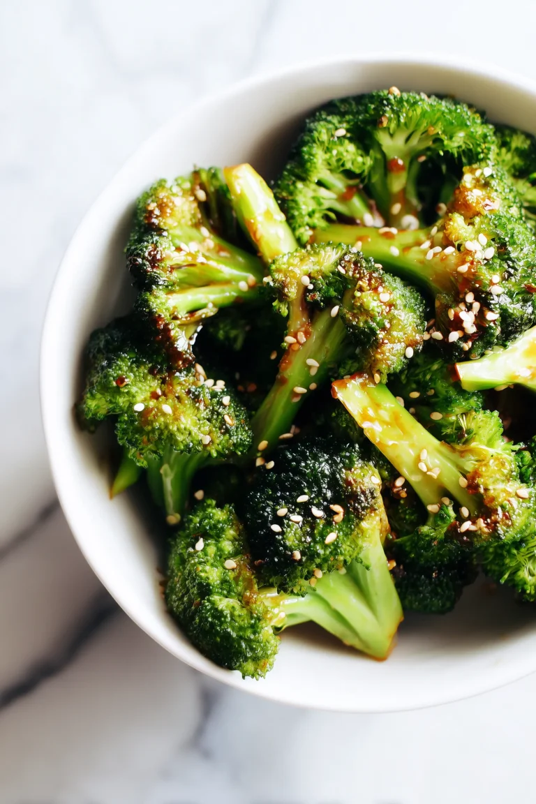 A close-up of Ginger-Garlic Roasted Broccoli with sesame seeds, glistening on white marble.