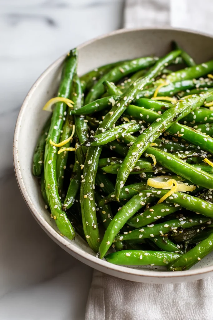 Honey Garlic Green Beans 4 Dish of Honey Garlic Green Beans with sesame seed garnish and lemon zest on a bright table.