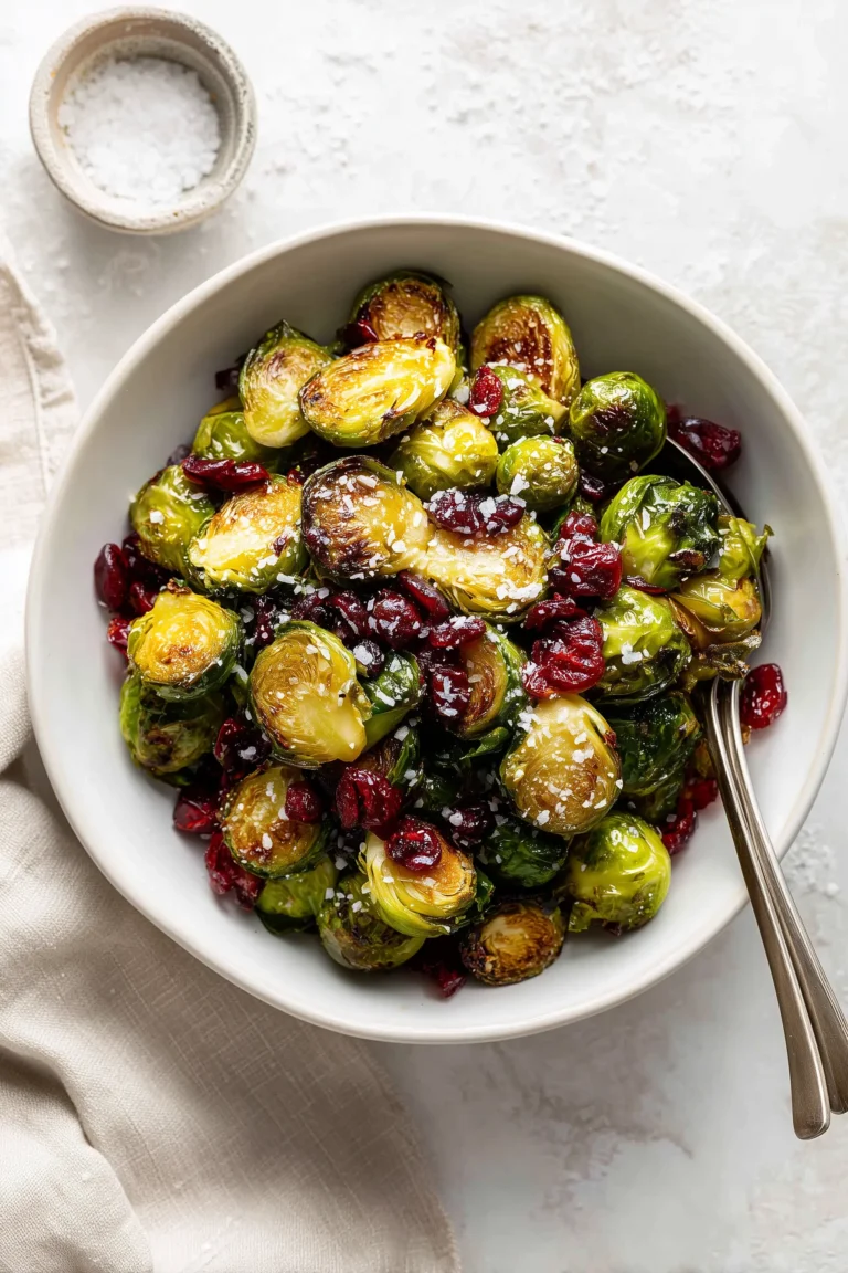 Overhead view of roasted Brussels sprouts mixed with cranberries in a white bowl, on a light background.