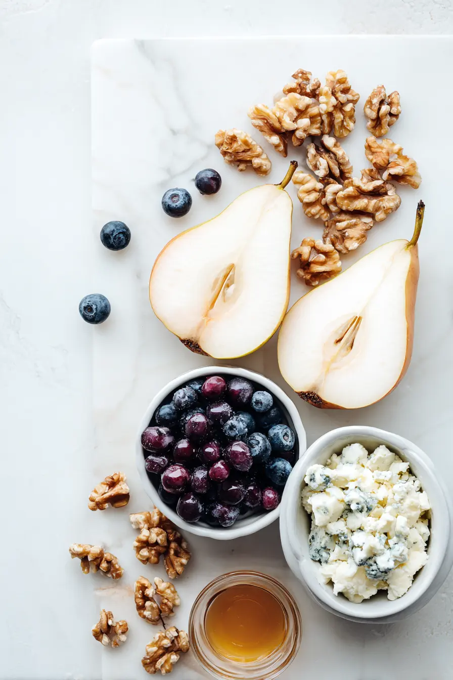 Baked Pears with Berries, Honey, Walnuts & Blue Cheese (Cozy, Easy Dessert) 2 Overhead view of pears, berries, honey, walnuts, and blue cheese arranged on white marble as ingredients for Baked Pears with Berries, Honey, Walnuts & Blue Cheese.