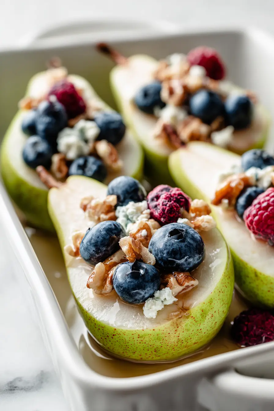 Baked Pears with Berries, Honey, Walnuts & Blue Cheese (Cozy, Easy Dessert) 3 White baking dish filled with pear halves topped with berries, honey, walnuts, and blue cheese, showing the preparation step for Baked Pears with Berries, Honey, Walnuts & Blue Cheese.