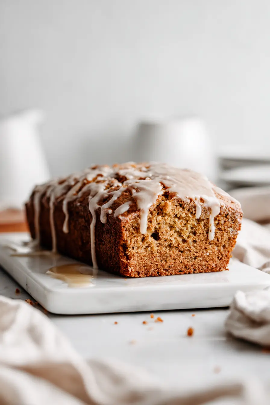 Whole Spiced Zucchini Sweet Potato Cake loaf with maple glaze dripping down the sides on a white platter over white marble.